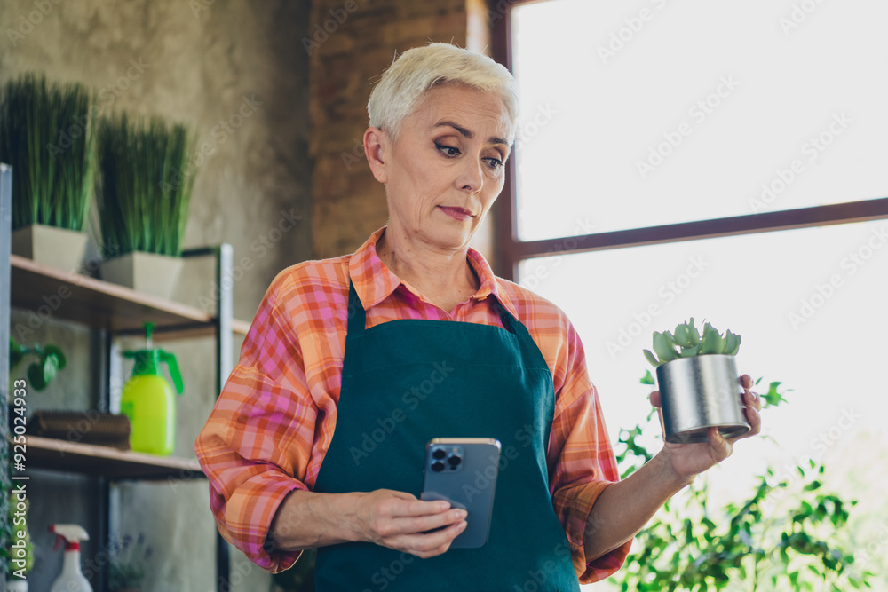 Sticker photo of doubtful unsure elderly lady wear apron enjoying gardering reading modern device indoors ho