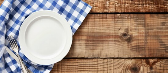 White plate on wooden table with blue checkered napkin. Flat lay, top view, with ample copy space image.