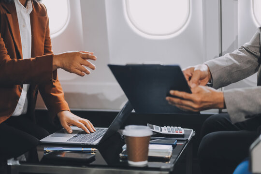 business people at meeting in private plane, Asian businessman in suit is talking to woman in jet and pointing at blank laptop screen, colleagues are discussing deal and flying in plane - Powered by Adobe