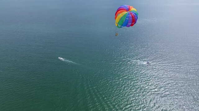Drone video of a colorful parasail soaring over the open ocean, towed by a speedboat below. The aerial view captures the thrill and freedom of parasailing against a vast, serene seascape