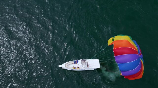 Drone video of a colorful parasail being towed by a speedboat over the ocean. The scene captures the excitement of parasailing with stunning views of the coastline and open sea