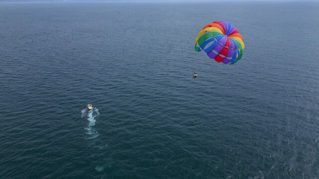 Drone video of a colorful parasail soaring over the open ocean, towed by a speedboat below. The aerial view captures the thrill and freedom of parasailing against a vast, serene seascape