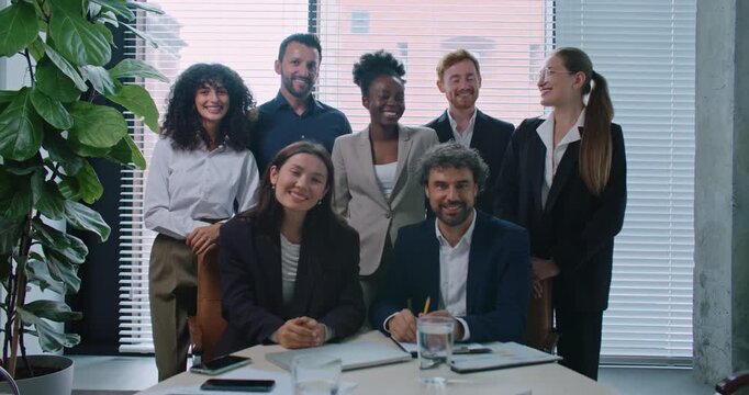 Camera moving closer to multi-ethnic group of people gathering together behind table. Talking with each other. Looking directly at camera while smiling. Growing business. Team building. Diversity