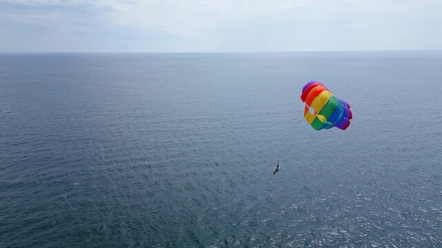 Drone video of a colorful parasail soaring over the open ocean, towed by a speedboat below. The aerial view captures the thrill and freedom of parasailing against a vast, serene seascape