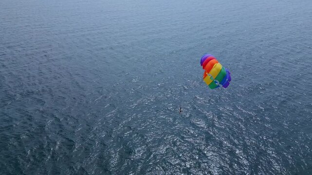 Drone video of a colorful parasail soaring over the open ocean, towed by a speedboat below. The aerial view captures the thrill and freedom of parasailing against a vast, serene seascape