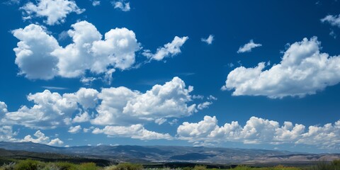 A beautiful landscape showing a bright blue sky filled with scattered fluffy clouds, expanding over scenic mountains.