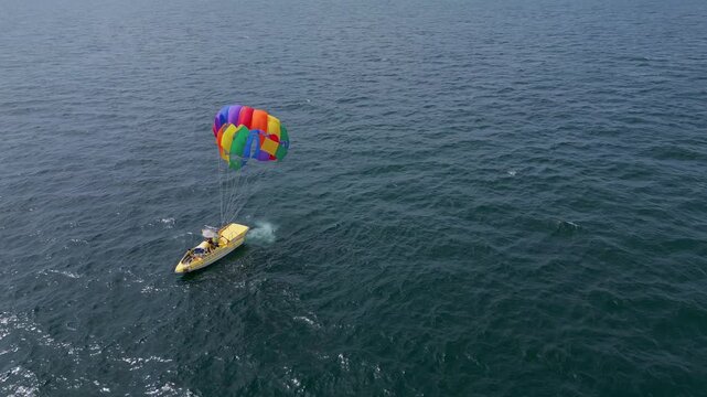 Drone video of a colorful parasail being towed by a speedboat over the ocean. The scene captures the excitement of parasailing with stunning views of the coastline and open sea