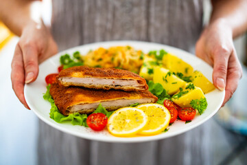 Crispy breaded fried pork chop, boiled potatoes and sauerkraut salad served on white plate on wooden table 
