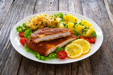 Crispy breaded fried pork chop, boiled potatoes and sauerkraut salad served on white plate on wooden table 