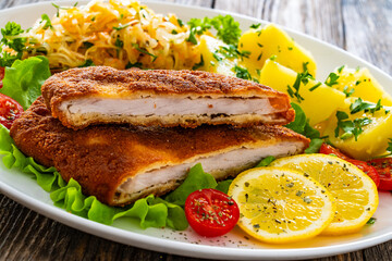 Crispy breaded fried pork chop, boiled potatoes and sauerkraut salad served on white plate on wooden table 
