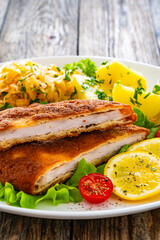 Crispy breaded fried pork chop, boiled potatoes and sauerkraut salad served on white plate on wooden table 