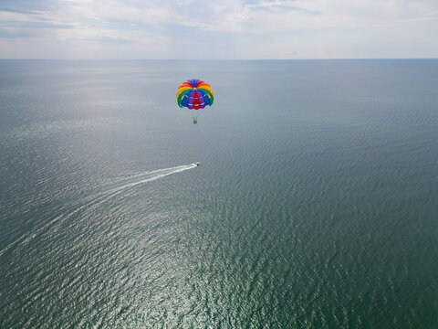 Drone video of a colorful parasail soaring over the open ocean, towed by a speedboat below. The aerial view captures the thrill and freedom of parasailing against a vast, serene seascape