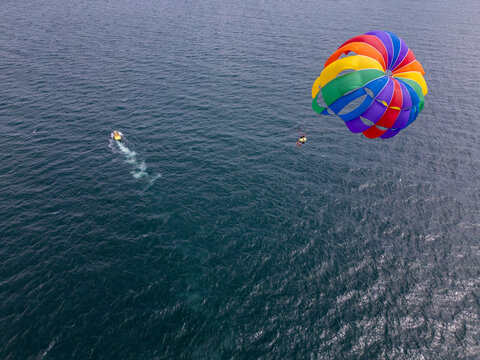 Drone video of a colorful parasail soaring over the open ocean, towed by a speedboat below. The aerial view captures the thrill and freedom of parasailing against a vast, serene seascape