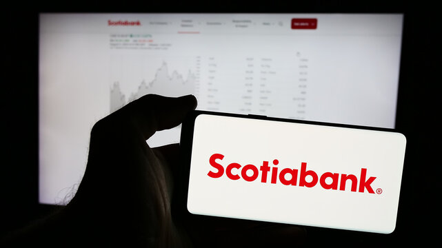 Stuttgart, Germany - 08-12-2024: Person holding mobile phone with logo of financial company Bank of Nova Scotia (Scotiabank) in front of business web page. Focus on phone display.