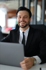Fototapeta premium A man in a suit and tie is smiling and holding a laptop. He is happy and confident