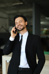 A man in a suit is talking on his cell phone while smiling. He is dressed professionally and he is in a good mood