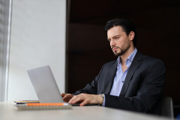 A man in a suit is typing on a laptop computer. He is focused on his work, possibly a business meeting or a project. Concept of professionalism and productivity, as the man is dressed in a suit