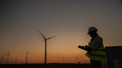 women engineer working and holding the report at wind turbine farm Power Generator Station on mountain,Thailand people