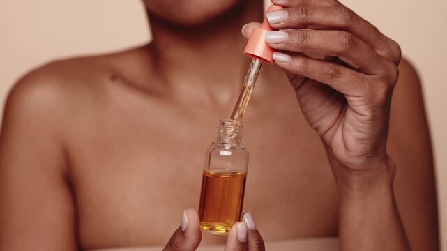 Close-up of a serene black woman using a dropper to apply serum oil skincare routine, symbolizing wellness and self-care.