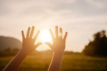 Close up of dreaming child pulls hands to sun. Religion helping hand. Unknown kid enjoy beautiful summer nature during epic warm sunset or sunrise. Prayer in religion concept