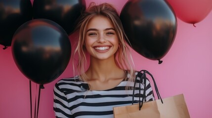 Naklejka premium A girl smiles brightly, holding black balloons and a shopping bag against a pink backdrop
