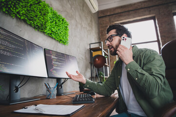 Portrait of professional hacker young man speak phone computer desk loft interior office indoors