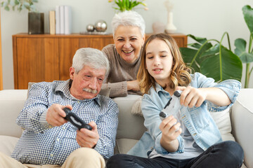 Happy family at home. Old senior man grandfather woman grandmother girl granddaughter playing video game with joysticks at home. Grandparent teenager two generations using gamepads for video game