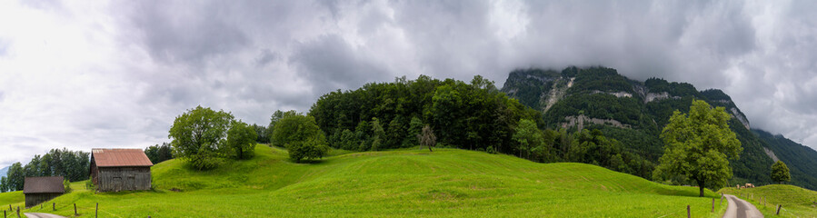 Panorama with old farmhouse on steep slope and rocky mountain in background. green pasture and...