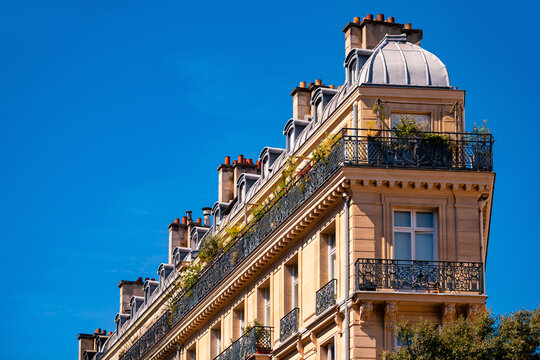 Flat iron-shaped residential building in Paris (France) with wrought-iron balustrades, sandstone façade and tin roof on a sunny day. Typical building on the large boulevards of the french metropolis.