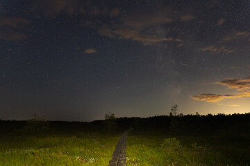 Fototapeta premium Hiking wooden trail in the Pikanomme swamp at night. Starry sky and milky way. Nature of Estonia.