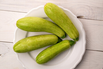 Four ripe zucchini with a ceramic plate on a wooden table, macro, top view.