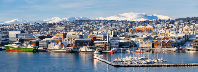 Panorama of norwegian city of Tromso in the winter. Snowy roofs, embankment near the port and fishing ships, Sunny winter day.