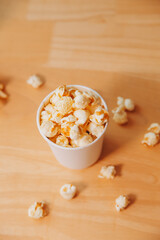A bucket of popcorn, top-view, warm colors, light brown wooden background, flat lay, daylight macro close-up