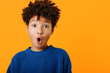 Astonished young african american boy making a comical expression against a bright orange...
