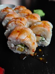 Sushi on a black background. Roll covered with juicy sauce.