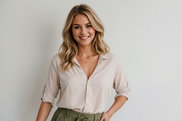 Lady with a radiant smile in a white shirt and olive trousers against plain backdrop 