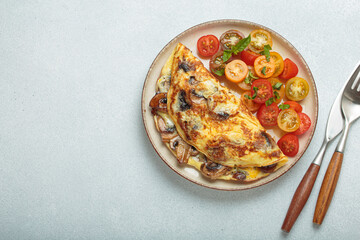 Delicious omelette with roasted mushrooms served with fresh cherry tomatoes and basil on blue background for healthy breakfast or lunch from above, space for text