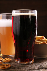 Glasses of beer, pretzel crackers and rusks on wooden table, closeup