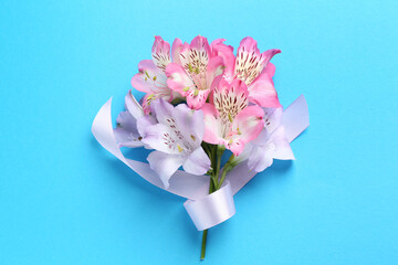 Beautiful alstroemeria flowers and ribbon on light blue background, top view