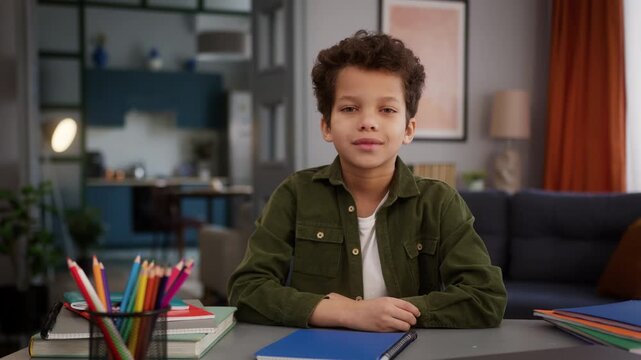 African American ethnic little son boy baby child kid schoolboy pupil at home distant education e-learning study learn studying learning smiling looking at camera indoors at table homework course