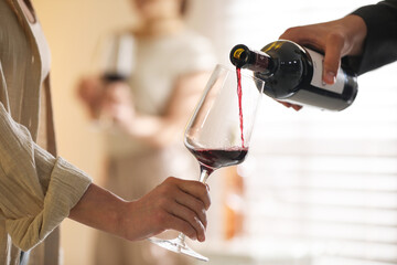 Man pouring red wine into woman`s glass indoors, selective focus