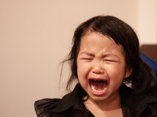 Crying asian toddler expressing strong emotions indoors