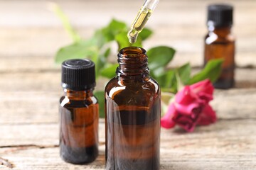 Essential oil dripping from pipette into bottle at table, closeup