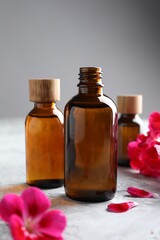 Bottles of geranium essential oil and beautiful flowers on light grey textured table, closeup