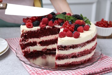 Woman cutting tasty sponge cake with different berries and mint at light grey table, closeup