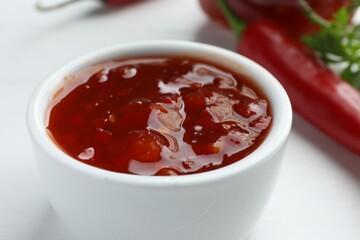 Spicy chili sauce in bowl on white table, closeup