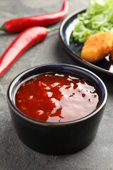 Spicy chili sauce in bowl on grey textured table, closeup