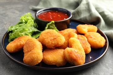 Tasty chicken nuggets with chili sauce and lettuce on grey table, closeup