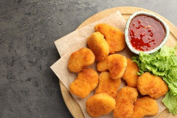 Board with hot chili sauce, lettuce and nuggets on grey textured table, top view. Space for text