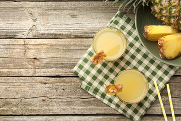 Tasty pineapple juice in glasses and fresh fruit on wooden table, flat lay. Space for text
